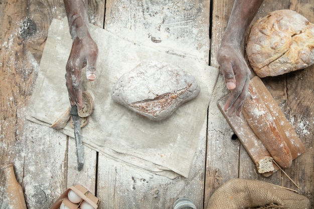 Vista dall'alto dell'uomo afro-americano cuochi cereali freschi, pane, crusca sulla tavola di legno