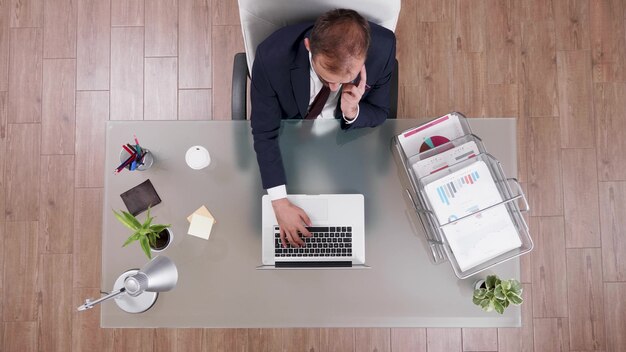 Vista dall'alto dell'uomo d'affari in tuta che discute di profitto online con il manager al telefono