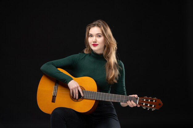 Vista dall'alto della bella ragazza bionda che suona la chitarra sul nero