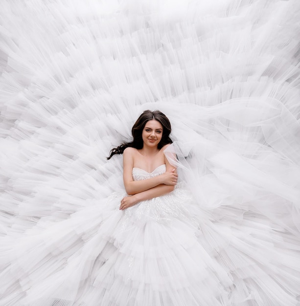 Vista dall'alto della bella ragazza sposa modello bruna sdraiata su un abito da sposa bianco gonfio con spalle aperte Elegante signora vestita in abito stile principessa