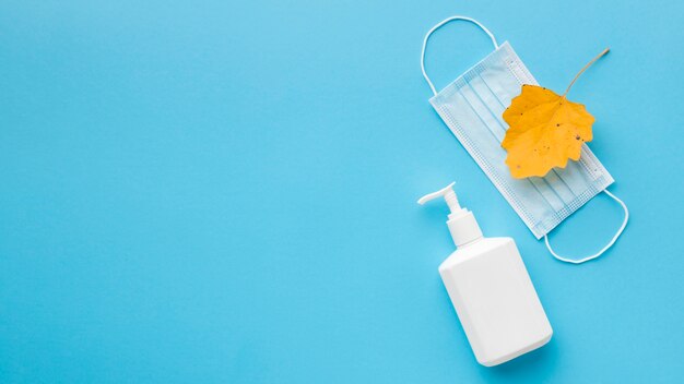 Vista dall'alto della bottiglia di sapone liquido con maschera medica e foglia d'autunno