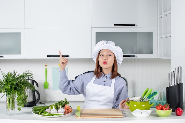 Vista dall'alto della chef donna sorpresa e verdure fresche che puntano verso l'alto sul lato destro nella cucina bianca