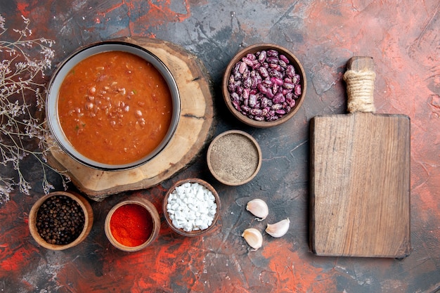 Vista dall'alto della classica zuppa di pomodoro sul vassoio in legno fagioli diverse spezie e tagliere marrone sulla tavola di colore misto
