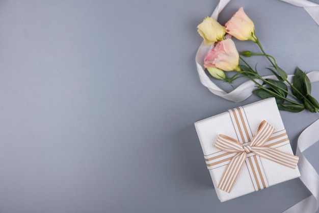 Vista dall'alto della confezione regalo e fiori con nastro su sfondo grigio con spazio di copia