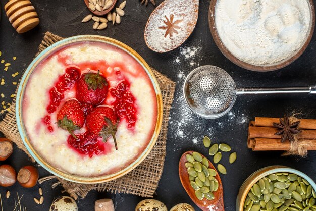 Vista dall'alto della deliziosa colazione servita con marmellata di fragole in una ciotola e farina di nocciole uova cucchiai su sfondo di colore scuro