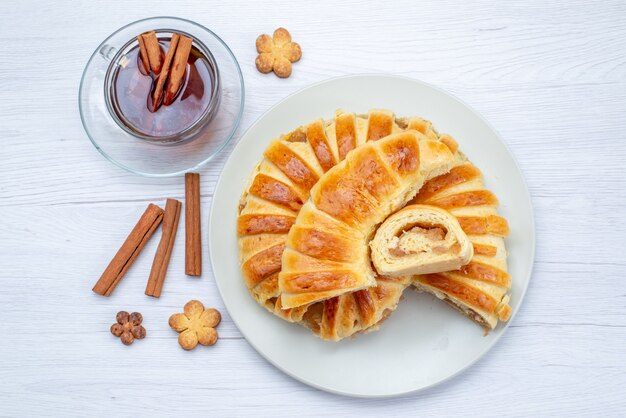 Vista dall'alto della deliziosa pasticceria al forno con ripieno dolce affettato e intero insieme a biscotti e tè sulla scrivania leggera, biscotto biscotto pasticceria dolce