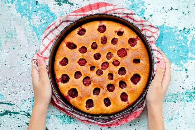 Vista dall'alto della deliziosa torta ai frutti di bosco cotta e gustosa all'interno della padella tenuta dalla femmina sul blu brillante, torta biscotto pasta frutta bacca dolce