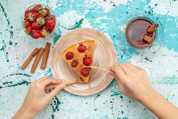 Vista dall'alto della deliziosa torta alla fragola affettata torta gustosa farsi mangiare con tè alla cannella e fragole rosse fresche sulla scrivania blu brillante, torta cuocere la pasta dolce