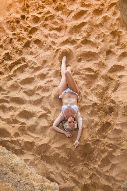 Vista dall'alto della donna che si distende sull'idilliaca spiaggia tropicale sdraiata sulla spiaggia sabbiosa mentre le onde schizzano su di essa