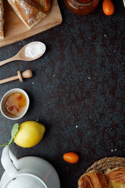 Vista dall'alto della farina di croissant kumquat al limone con marmellata con teiera su sfondo nero