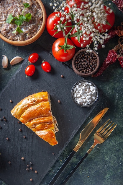 Vista dall'alto della fetta di torta di carne gustosa con pomodori rossi e carne ripiena sulla superficie scura