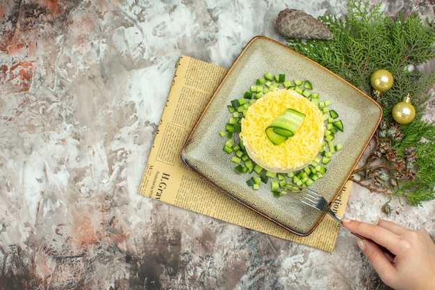 Vista dall'alto della forchetta che regge la mano su una gustosa insalata servita con cetriolo tritato e forchetta coltello su un vecchio giornale