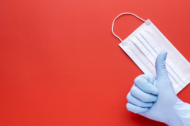 Vista dall'alto della mano che dà i pollici in su con maschera medica e copia spazio