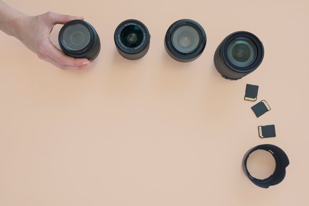 Vista dall&#39;alto della mano della persona che organizza l&#39;obiettivo della fotocamera; scheda di memoria e anelli di prolunga su sfondo colorato