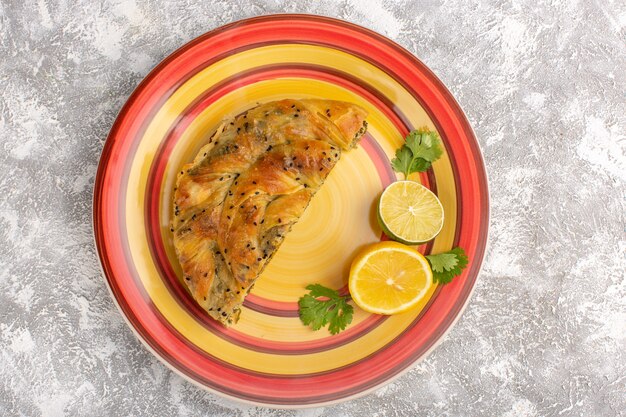 Vista dall'alto della pasticceria con farina di pasta deliziosa a base di carne all'interno del piatto affettato con limone su superficie bianco chiaro