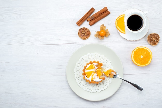 Vista dall'alto della piccola torta con crema e arance affettate insieme a una tazza di caffè e cannella sulla scrivania leggera, torta di frutta biscotto dolce