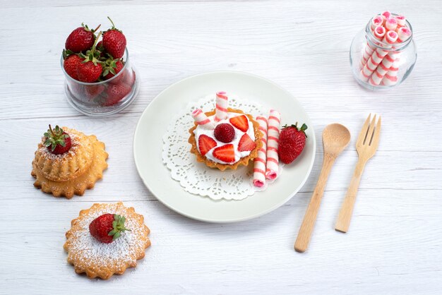 Vista dall'alto della piccola torta con crema e fragole a fette torte caramelle su bianco, zucchero dolce bacca torta di frutta