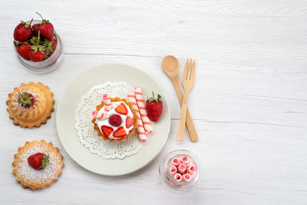 Vista dall'alto della piccola torta con crema e fragole a fette torte caramelle su bianco, zucchero dolce torta di frutta