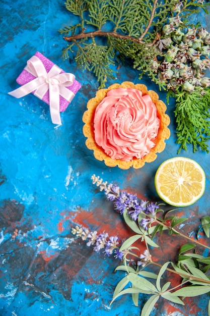 Vista dall'alto della piccola torta con crema pasticcera rosa fetta di limone ramo di albero sulla superficie blu