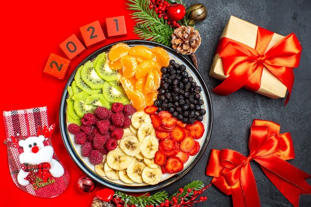 Vista dall'alto della raccolta di frutta fresca sugli accessori della decorazione del piatto della cena rami di abete e numeri su un tovagliolo rosso e nastro rosso e regalo