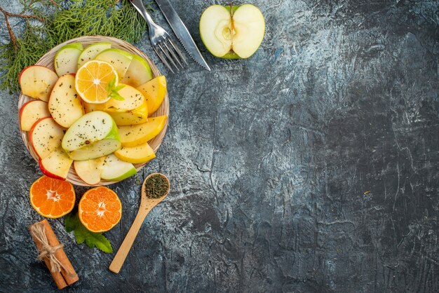 Vista dall'alto della raccolta di frutti organici naturali freschi su un piatto bianco posate con rami di abete lime cannella su uno sfondo scuro