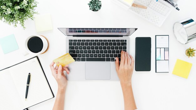 Vista dall'alto della signora asiatica freelance utilizzando laptop shopping online con carta di credito sul tavolo