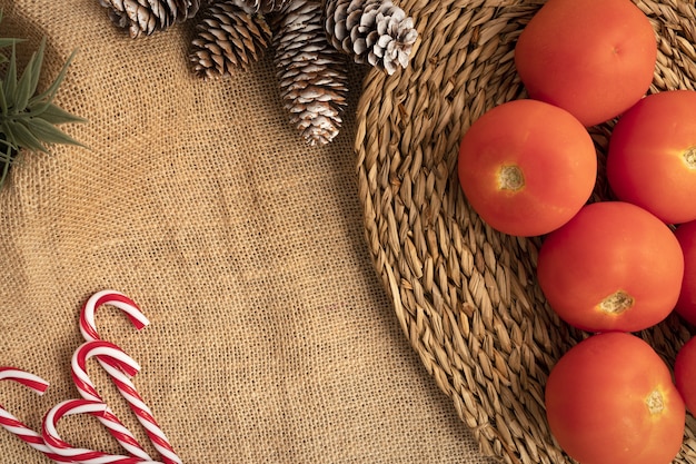 Vista dall'alto della tavola di Natale con pomodori, bastoncini di zucchero e pigne