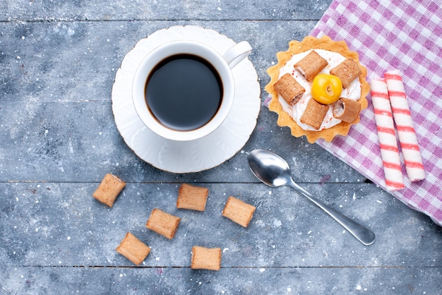 Vista dall'alto della tazza di caffè con biscotti a forma di cuscino e torta cremosa su grigio, pasta dolce biscotto al caffè