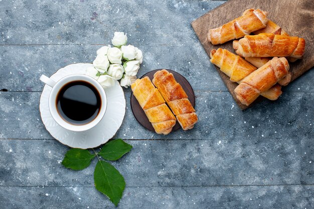 Vista dall'alto della tazza di caffè insieme a braccialetti deliziosi dolci su torta di pasticceria grigia e dolce