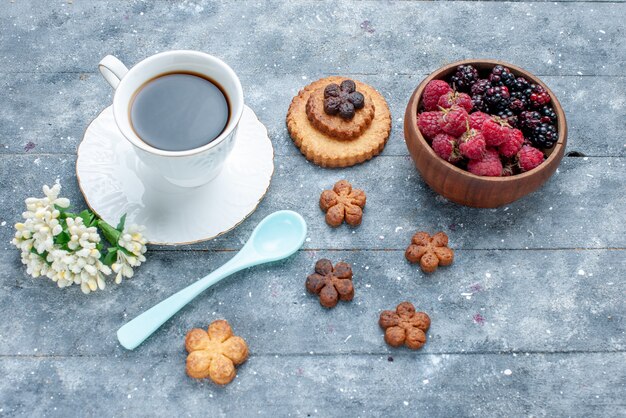 Vista dall'alto della tazza di caffè insieme a piccoli biscotti e frutti di bosco freschi su legno grigio, zucchero dolce cuocere il biscotto di pasticceria biscotto
