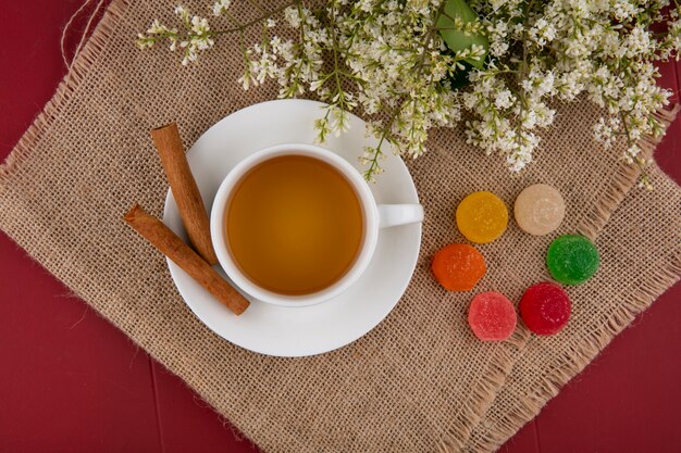 Vista dall'alto della tazza di tè con marmellate color cannella e fiori su un tovagliolo beige