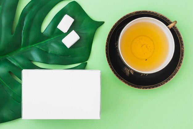 Vista dall&#39;alto della tazza di tisana con cubetti di zucchero e scatola bianca su sfondo verde