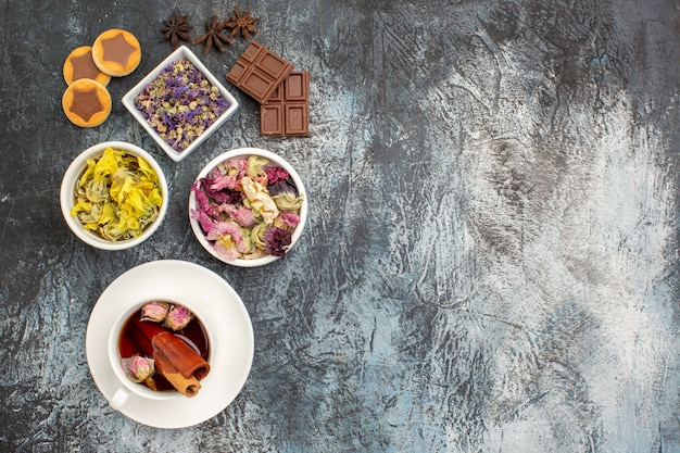 Vista dall'alto della tisana con fiori secchi e biscotti e barrette di cioccolato e anice su fondo grigio