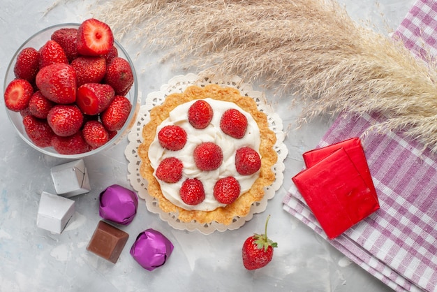 Vista dall'alto della torta cremosa con fragole rosse fresche e torta di caramelle al cioccolato sulla scrivania a luce bianca, torta di frutta e bacche di biscotti alla crema dolce