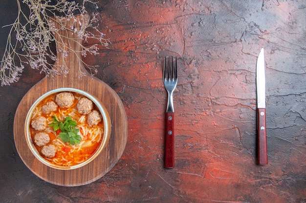 Vista dall'alto della zuppa di polpette di pomodoro con noodles in una ciotola marrone sul lato destro dello sfondo scuro