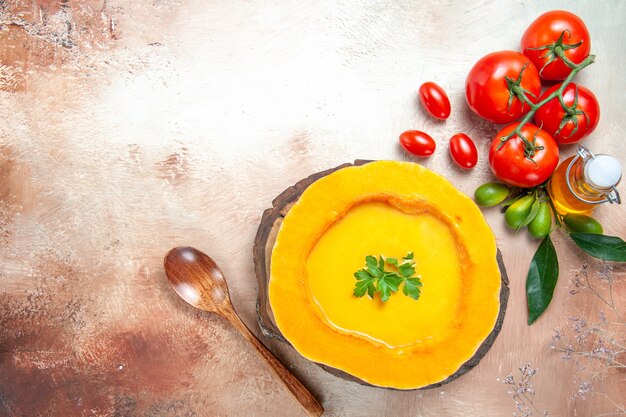 Vista dall'alto della zuppa di zucca zuppa sul cucchiaio di bordo pomodori agrumi con foglie di olio