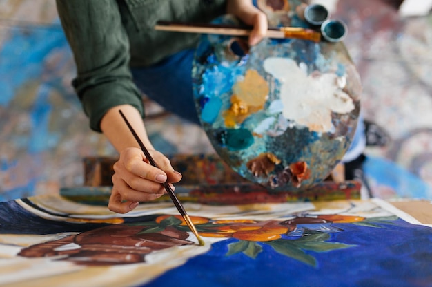 Vista dall'alto delle mani di una donna attraente che disegnano un'immagine straordinaria su tela in un moderno laboratorio d'arte accogliente