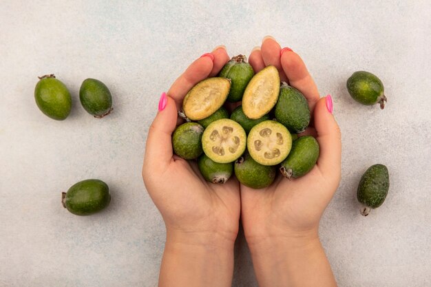 Vista dall'alto delle mani femminili che tengono una metà matura tropicale e interi feijoas con feijoas isolati su una superficie grigia