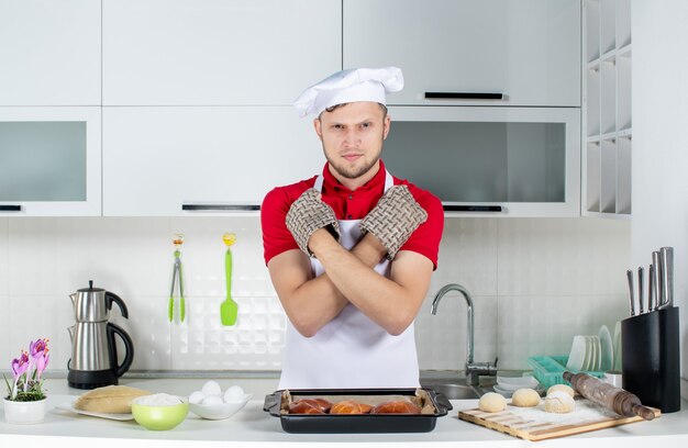 Vista dall'alto dello chef maschio nervoso che indossa il supporto in piedi dietro il tavolo con le uova di pasticceria grattugiate su di esso e facendo un gesto di arresto nella cucina bianca