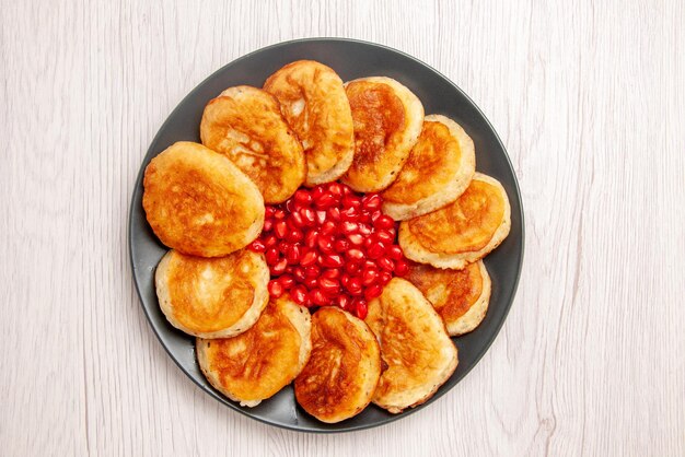 Vista dall'alto dessert appetitosi frittelle e semi di melograno sul piatto nero sul tavolo bianco