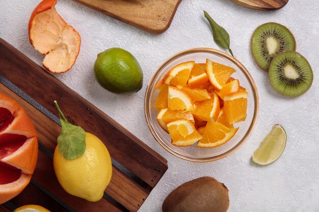 Vista dall'alto di agrumi come fette d'arancia in una ciotola con limone e pompelmo con kiwi su sfondo bianco