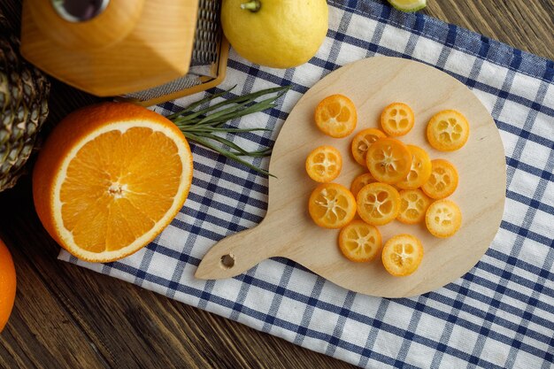 Vista dall'alto di agrumi come fette di kumquat sul tagliere e scalogno arancione tagliato al limone con grattugia su tela a quadri su fondo di legno
