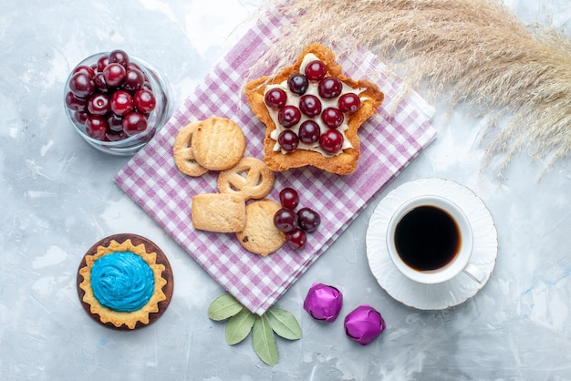 Vista dall'alto di amarene fresche all'interno del piatto con torta cremosa a forma di stella, tè e biscotti su biscotto leggero, torta di frutta acida