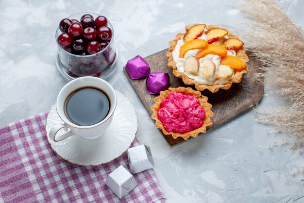 Vista dall'alto di amarene fresche all'interno di una piccola tazza di vetro con torte alla crema e tè su luce bianca, frutta a bacca acida vitamina dolce