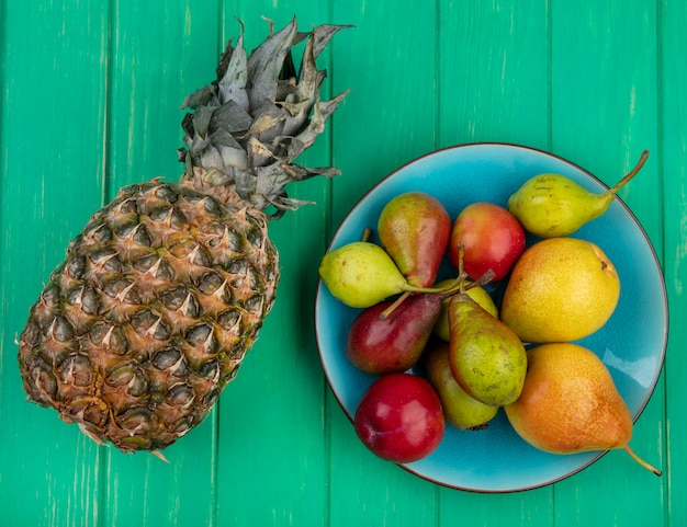 Vista dall'alto di ananas con pesche nel piatto sulla superficie verde