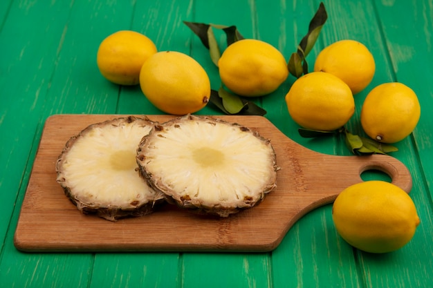 Vista dall'alto di ananas tritato succoso su una tavola di cucina in legno con limoni isolato su una parete di legno verde