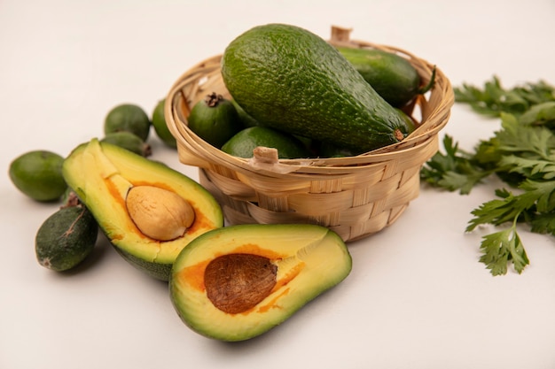 Vista dall'alto di avocado freschi luminosi su un secchio con feijoas con mezzo avocado isolato su una superficie bianca