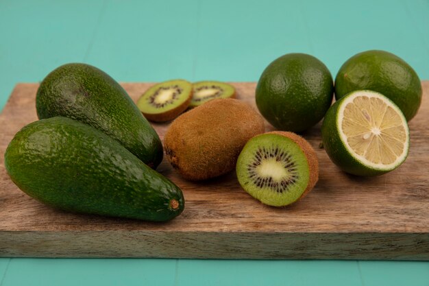 Vista dall'alto di avocado sani con lime e kiwi su una tavola da cucina in legno su una parete blu