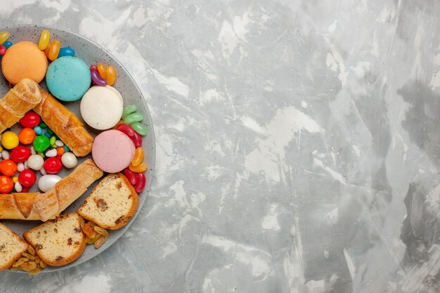 Vista dall'alto di bagel dolci con fette di torta macarons e caramelle sulla superficie bianca