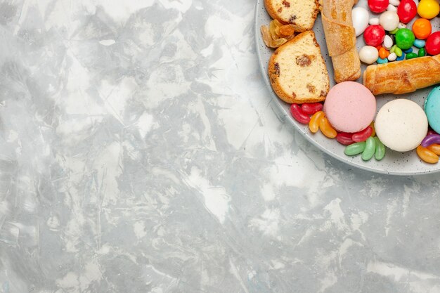 Vista dall'alto di bagel dolci con fette di torta macarons e caramelle sulla superficie bianca